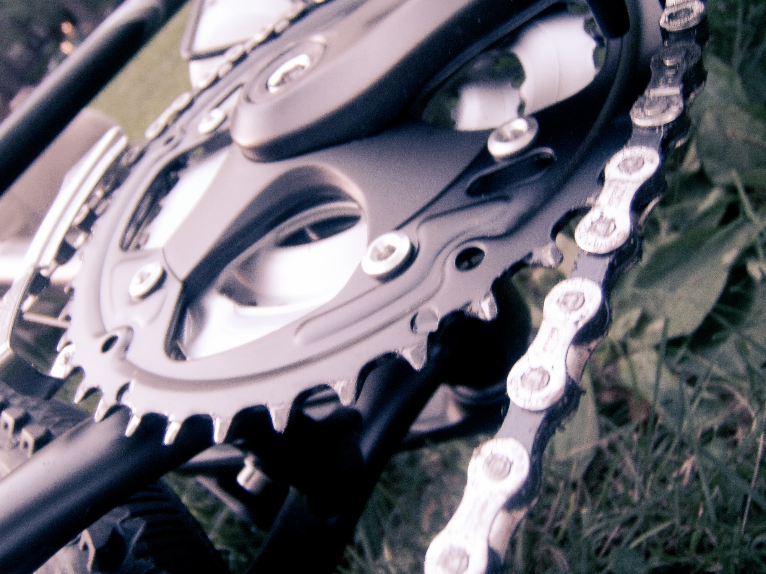 Close-up of a bicycle chainring with the crank arm attached, its teeth meshing with the links of a metal chain that wraps around the lower part of the chainring